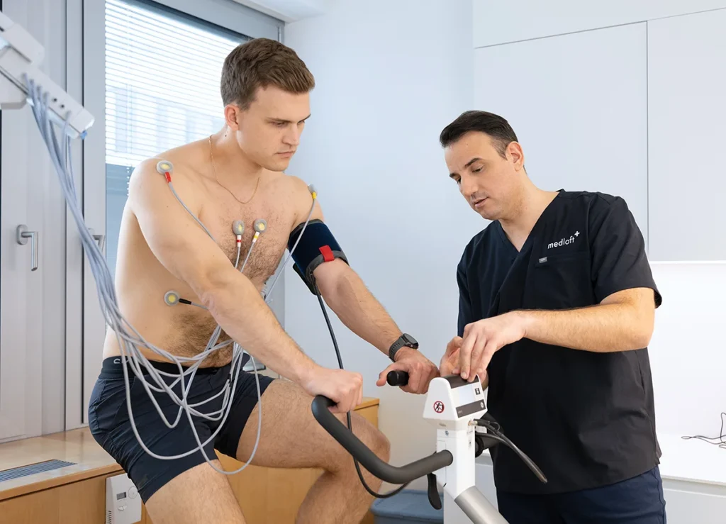 Auf dem Foto sehen wir OA Dr. Milos Tajsic, der sein Fachwissen und seine Fürsorge demonstriert, während er einem Patienten bei einem Belastungs-EKG unterstützt.