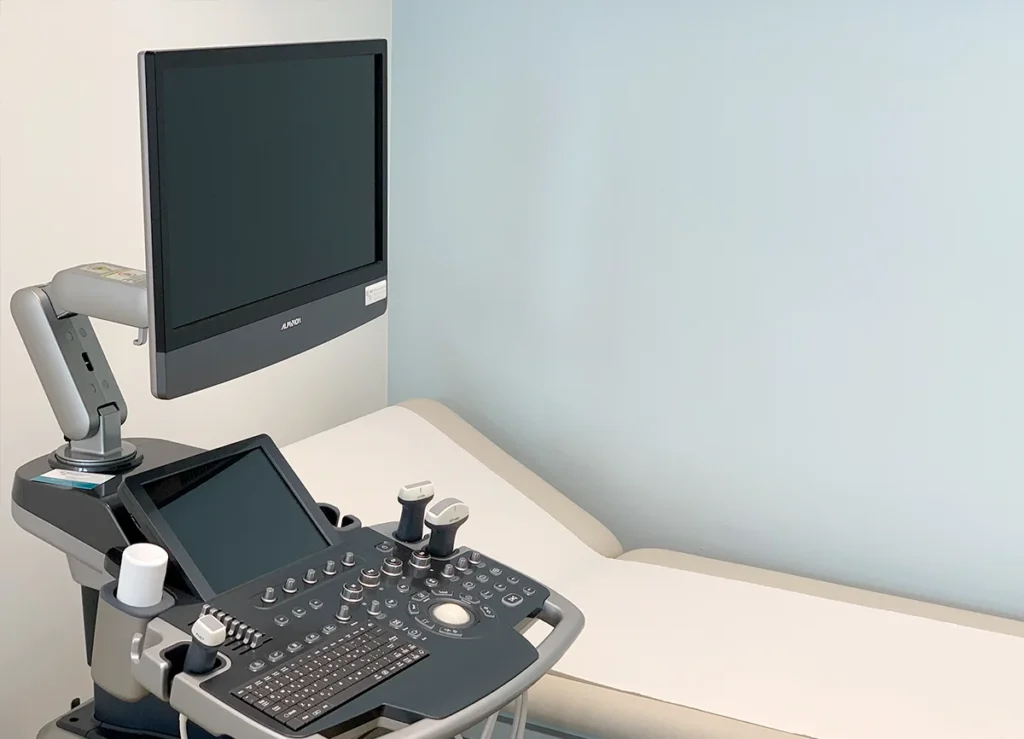 Ultraschallgerät für Echokardiographie mit Patientenliege im Hintergrund.